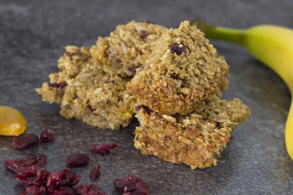 Vegan Fruity Flapjack Recipe (Healthy, Chewy Flapjacks) 150 fruity vegan flapjacks on a grey blackground with dried cranberries and a banana on the side