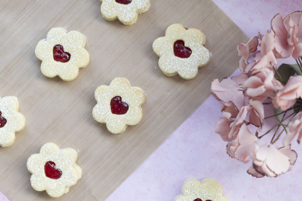 Homemade Vegan Jammy Dodgers Recipe 169 vegan jammy dodgers on a baking sheet with a pink background