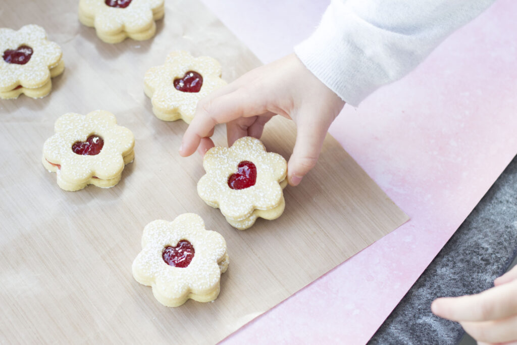 Homemade Vegan Jammy Dodgers Recipe 173 vegan jammy dodgers on a baking sheet, a young girl's hand picking one up
