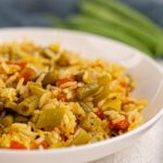 A close-up of a white plate filled with Vegan Biryani—rice mixed with green beans, tomatoes, and spices.