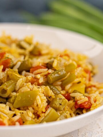 A close-up of a white plate filled with Vegan Biryani—rice mixed with green beans, tomatoes, and spices.