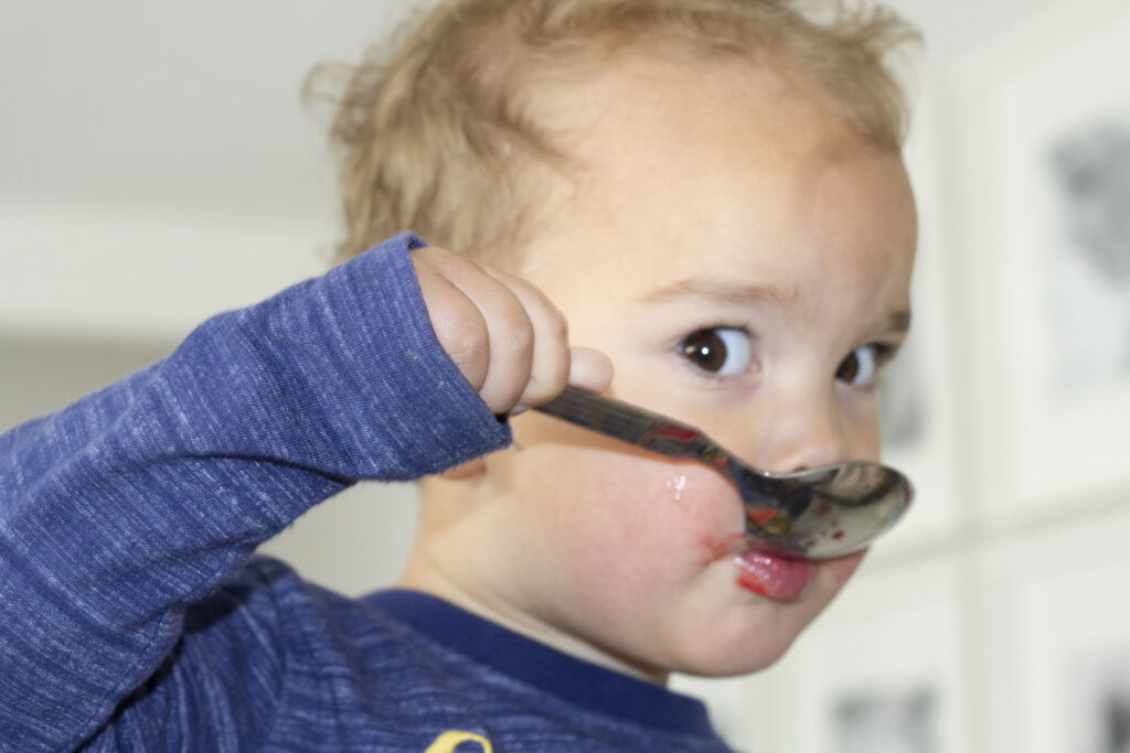 Easy Raspberry Sorbet Recipe (Homemade & Vegan) 140 a young child eating raspberry sorbet from a spoon