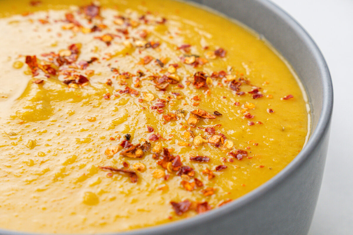 A close-up of a bowl filled with creamy, spicy Split Pea Soup, garnished with crushed red pepper flakes.
