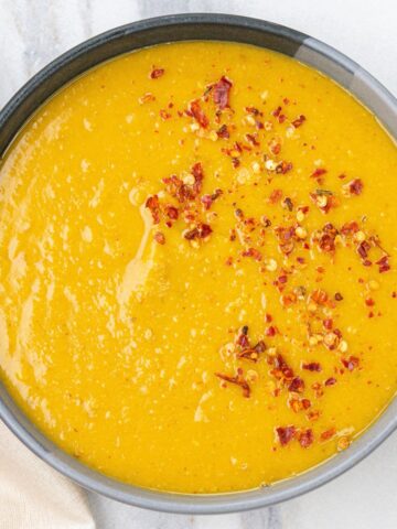 A bowl of creamy, spicy Split Pea Soup topped with crushed red pepper flakes sits on a light marble surface.