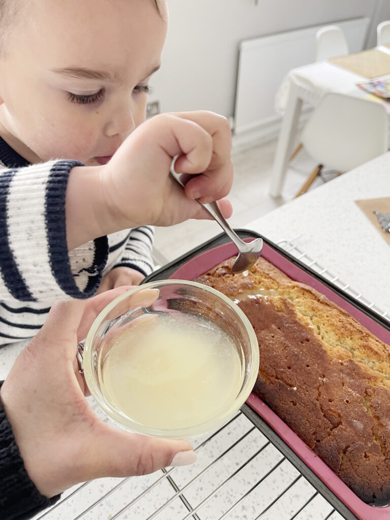 The Best Easy Vegan Lemon Drizzle Cake Recipe 216 a young boy spooning lemon syrup onto a lemon drizzle cake