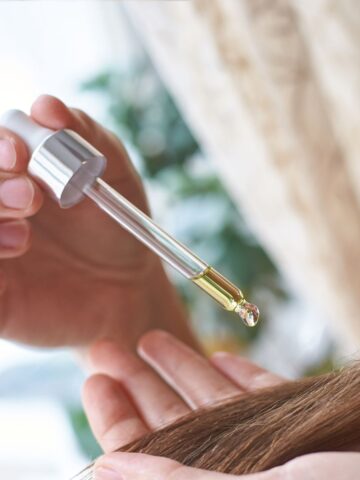 A person uses a dropper to apply a few drops of oil onto their hair, considering whether the keratin is vegan.
