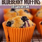 Close-up of vegan blueberry muffins in an orange wrapper with fresh blueberries, cooling on a wire rack. Text on the image reads "Best Ever Blueberry Muffins Vegan Recipe.