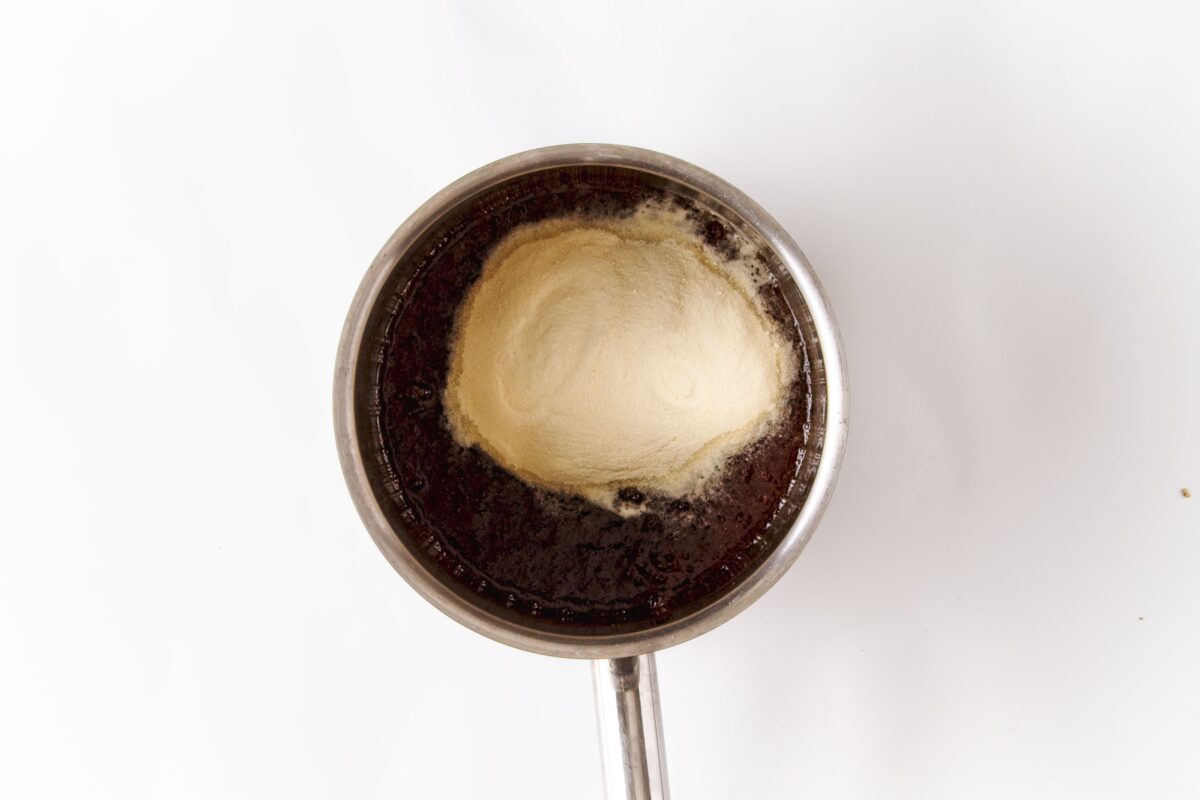 Vegan Strawberry and Cream Granola Protein Bars 218 Overhead view of a saucepan containing a dark liquid with a mound of powder on its surface, against a white background.
