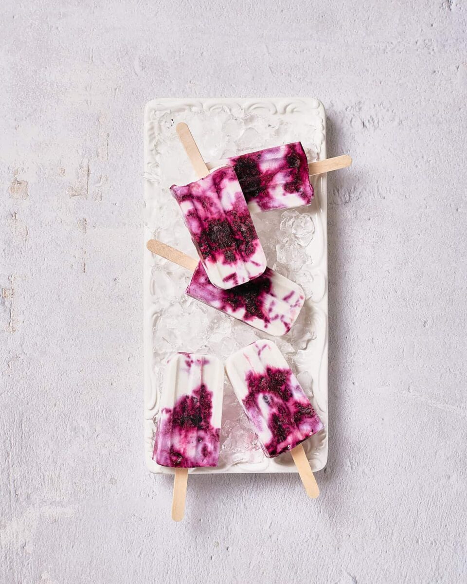 30 Delicious Vegan Blueberry Dessert Recipes 31 Homemade vegan blueberry popsicles served on ice on a white plate.