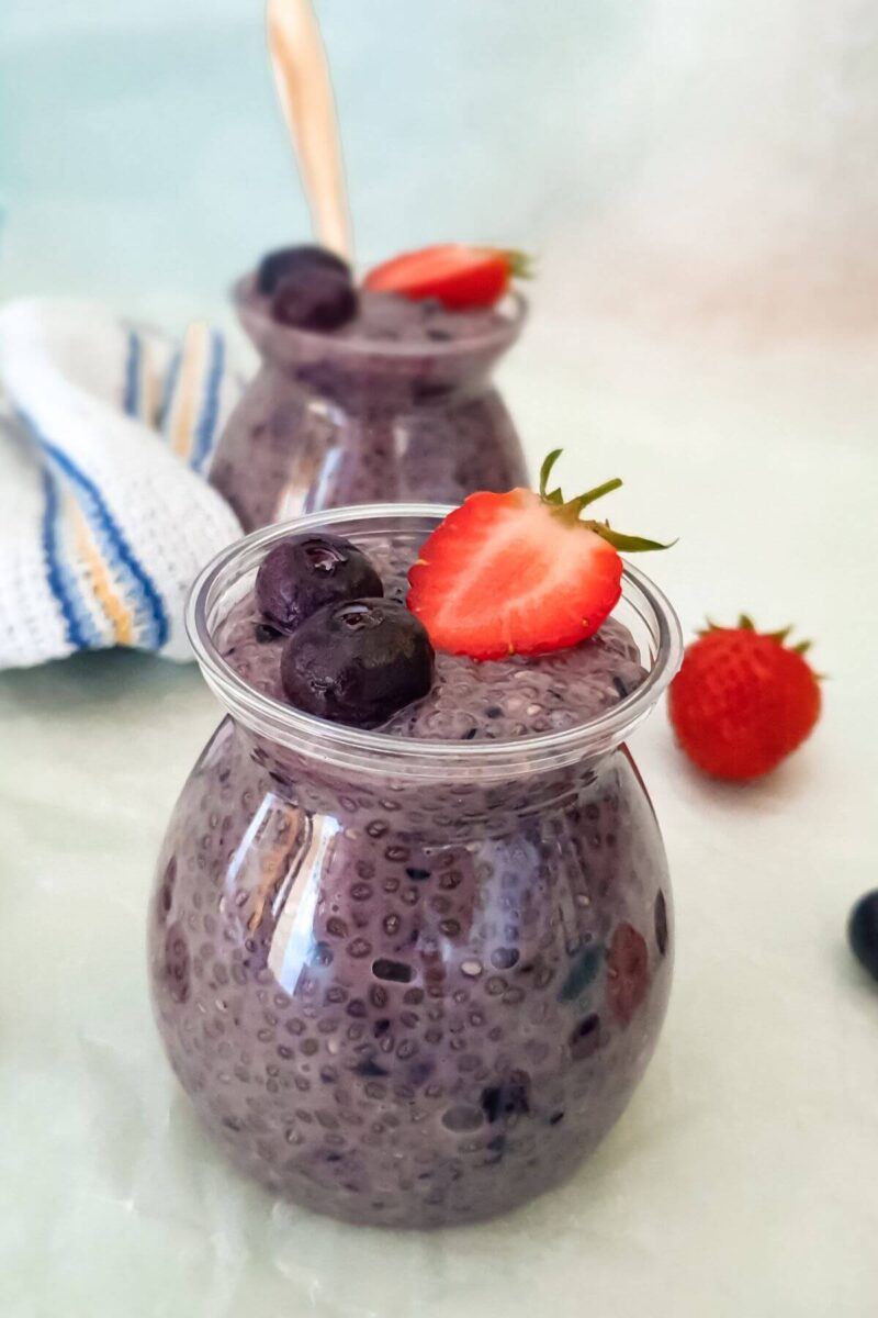 30 Delicious Vegan Blueberry Dessert Recipes 14 Jar of vegan blueberry chia seed pudding with fresh blueberries and strawberries in the background.