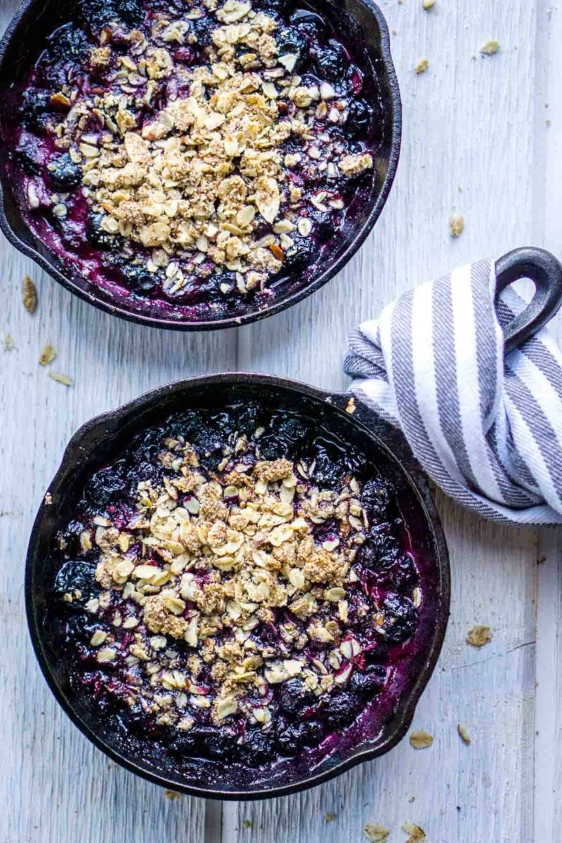 30 Delicious Vegan Blueberry Dessert Recipes 13 Two skillets of vegan blueberry crisp with a blue and white kitchen towel.