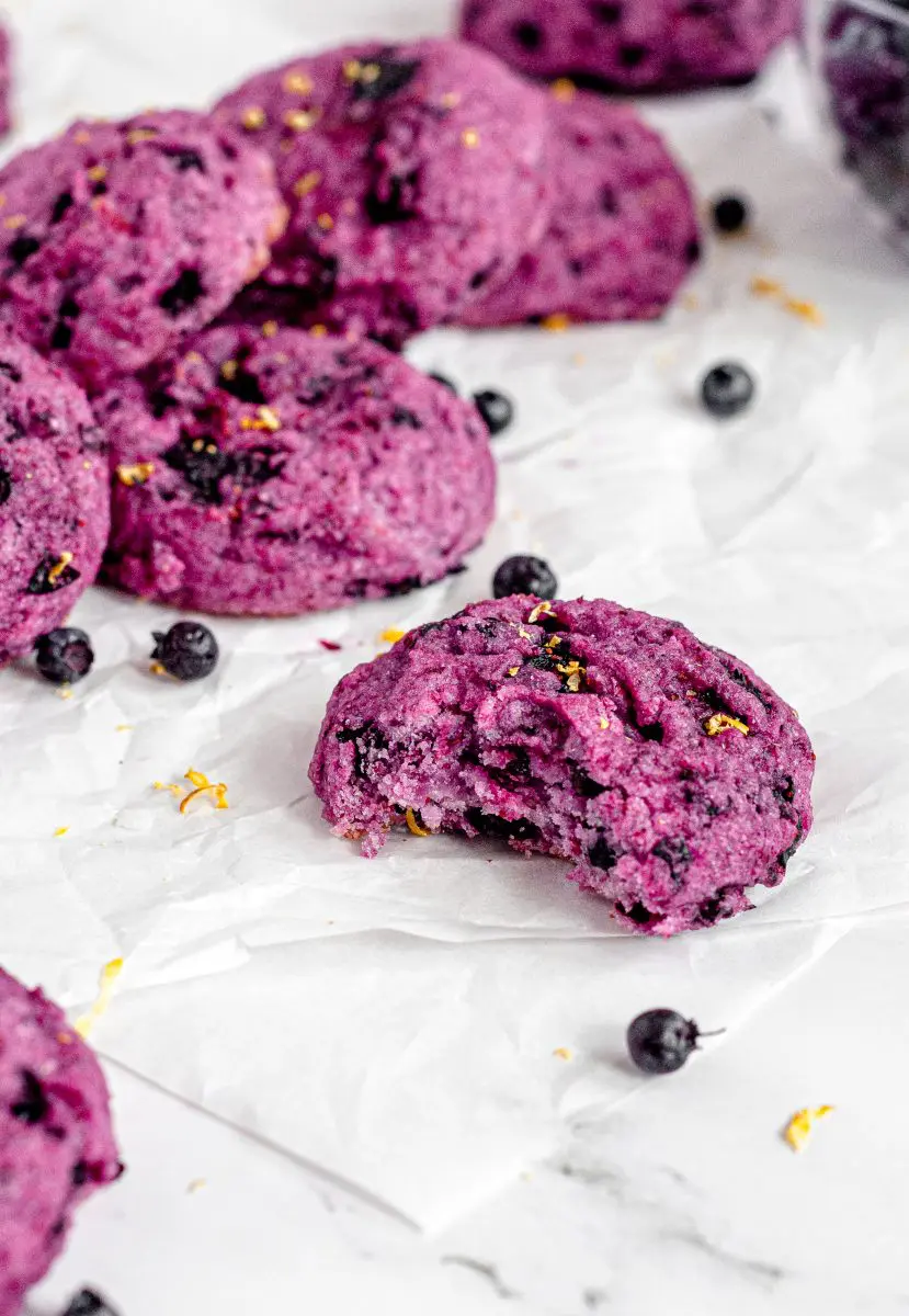 30 Delicious Vegan Blueberry Dessert Recipes 26 Vegan blueberry cookie with a bite taken out and a stack of cookies behind it.