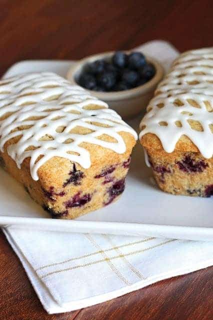 30 Delicious Vegan Blueberry Dessert Recipes 8 Two vegan lemon blueberry cakes on a tablecloth with a bowl of fresh blueberries in the background.