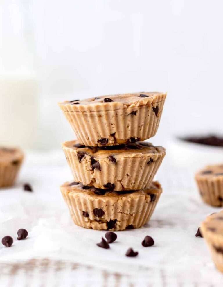 The Best High Protein Plant Based Snacks For On-The-Go 12 Three stacked chocolate chip cookie dough cups on a white surface, surrounded by scattered chocolate chips, offer a delicious twist. These high-protein, plant-based snacks are perfect for satisfying sweet cravings while fueling your body with nutritious goodness.