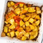 A white baking dish filled with lightly browned, seasoned roasted potato chunks and red bell pepper slices, perfect for a hearty vegan breakfast.