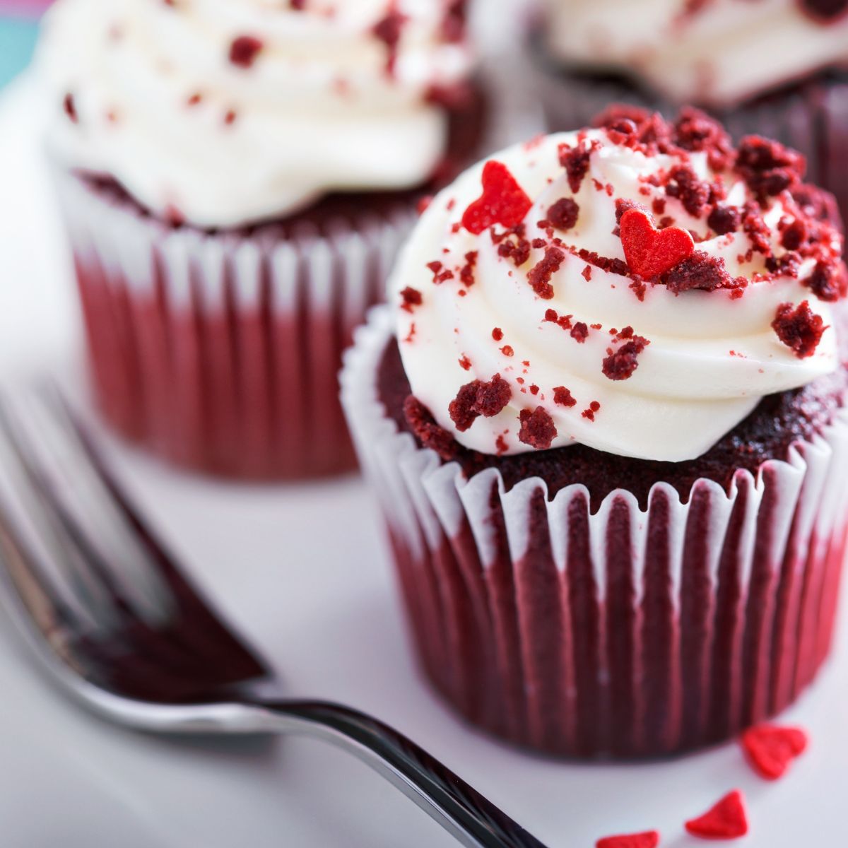 Red velvet cupcakes with white frosting, red crumbs, and small heart decorations next to a fork often spark curiosity about ingredients like Red 40—common in their vibrant hue. But is Red 40 vegan? Always check labels to be sure while indulging in these delightful treats!.
