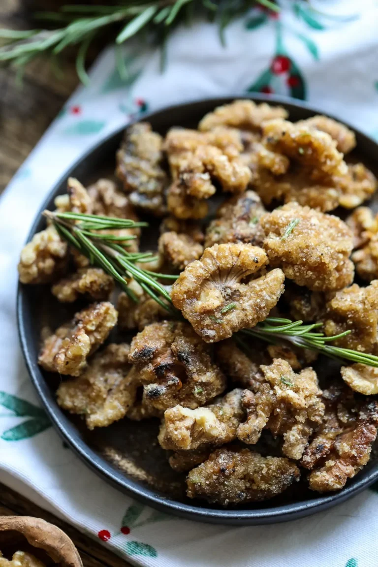The Best High Protein Plant Based Snacks For On-The-Go 13 A bowl filled with candied walnuts, high-protein plant-based snacks, garnished with sprigs of rosemary, placed on a patterned cloth.