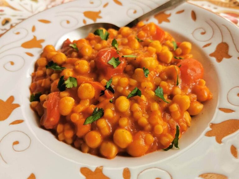 High Calorie Vegan Recipes - Meals For Weight Gain 15 A bowl of couscous stew with tomatoes, chickpeas, and garnished with chopped parsley. A spoon is placed on the edge of the bowl - a perfect example of high calorie vegan recipes for those aiming for weight gain.