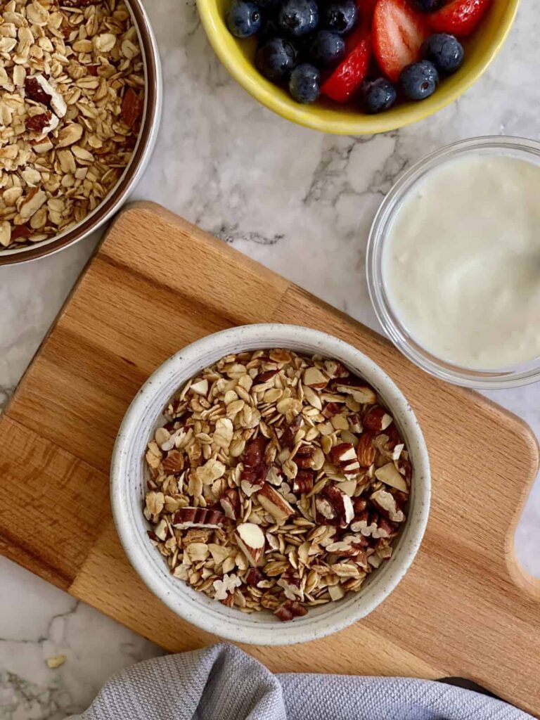 The Best High Protein Plant Based Snacks For On-The-Go 25 A bowl of granola is placed on a wooden board, with a bowl of mixed berries and a small container of yogurt nearby, perfect for a plant-based snack on-the-go.