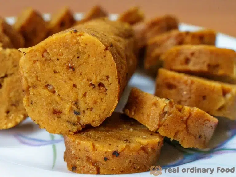 The Best High Protein Plant Based Snacks For On-The-Go 21 A sliced log of homemade vegan sausage on a white plate with a floral design. The high-protein, plant-based snack has a brownish color and coarse texture, with visible spices and ingredients, perfect for an on-the-go meal.