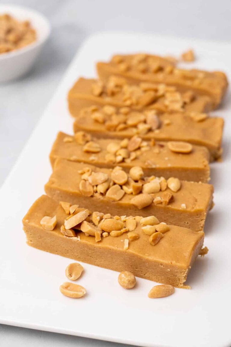 The Best High Protein Plant Based Snacks For On-The-Go 8 Rectangular peanut butter fudge pieces, enriched as high-protein snacks, topped with chopped peanuts on a white plate.