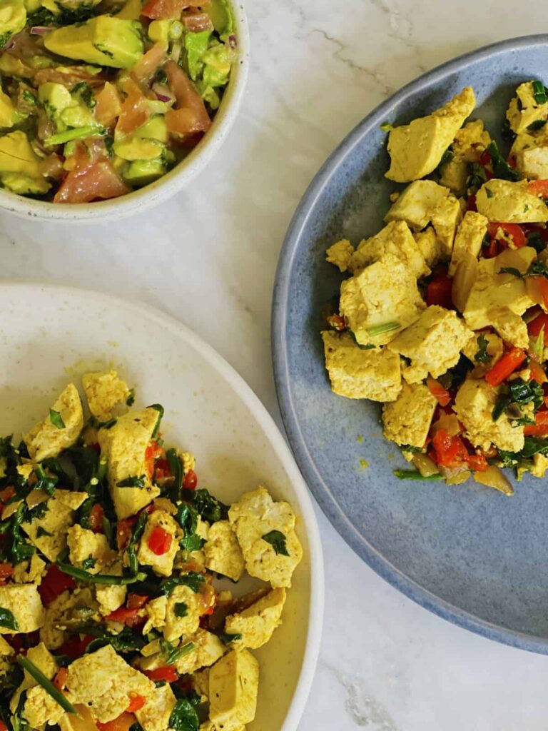 The Best High Protein Plant Based Snacks For On-The-Go 26 Plates of scrambled tofu with vegetables, a high-protein choice for plant-based snacks, sit next to a bowl of avocado salad on a marble countertop.