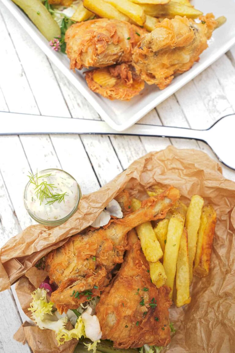 High Calorie Vegan Recipes - Meals For Weight Gain 13 Two portions of crispy fried chicken served with golden French fries. One portion is on a square white plate, and the other on crumpled brown paper, garnished with salad and a small glass of dipping sauce. Perfect for those exploring weight gain recipes.