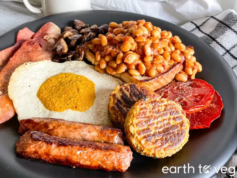High Calorie Vegan Recipes - Meals For Weight Gain 10 A high-calorie vegan breakfast plate featuring plant-based sausages, toast topped with baked beans, mushrooms, grilled tomatoes, hash brown patties, a sauce-topped egg substitute, and veggie bacon.