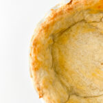 Close-up of a partially baked pie crust with golden edges in a white pie dish on a plain background.