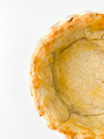 Close-up of a partially baked pie crust with golden edges in a white pie dish on a plain background.