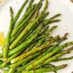A plate of roasted asparagus spears, perfectly cooked in the air fryer, garnished with red pepper flakes and accompanied by a lemon wedge.