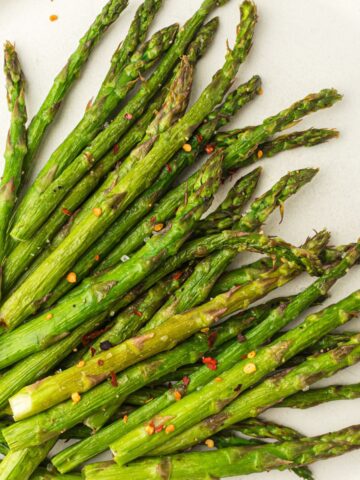 Roasted asparagus spears seasoned with chili flakes, prepared in an air fryer, and served on a white plate with a lemon wedge.