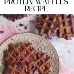 Plate of vegan dark chocolate waffles on a pink cloth, garnished with edible flowers, with a fork on the side.