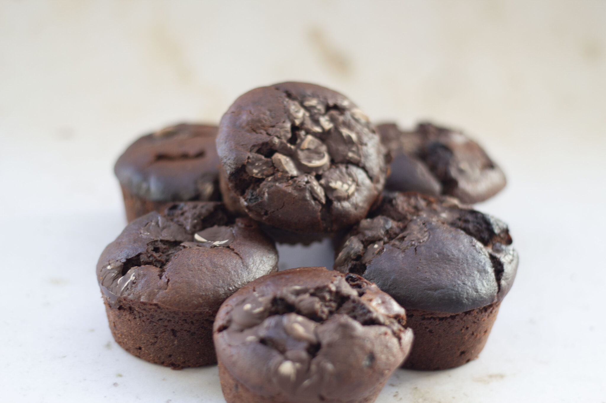 A group of six chocolate protein muffins rests on a white surface, with enticing chocolate chunks visible on top.