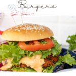 Savor a black bean and carrot burger stacked high with lettuce, tomato, and sauce on a sesame seed bun. Text: "Vegan Black Bean & Carrot Burgers" at the top and "wemadethisvegan.com" at the bottom.