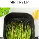 An air fryer basket brimming with perfectly cooked asparagus in an air fryer, accompanied by fresh lemon slices and vibrant leafy greens.