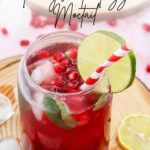 A glass of pomegranate fizz mocktail, garnished with vibrant pomegranate seeds, a fresh lime slice, and a playful striped straw, sits enticingly on the rustic wooden surface.