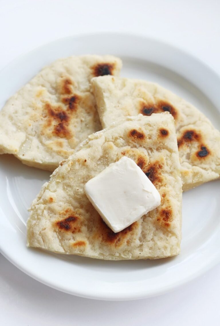 Vegan Irish Recipes For St Patrick's Day 13 Three pieces of flatbread on a white plate are topped with a pat of butter, making for a simple yet delightful treat, perfect for those seeking classic flavors during St. Patrick's Day.