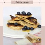 Plate of gluten-free oat flour pancakes topped with blueberries on a light surface. A fork and knife are placed nearby. Text above reads, "Vegan Oat Flour Pancakes - Get the recipe.