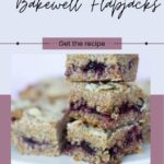 A stack of vegan cherry bakewell flapjacks graces a plate, surrounded by more delicious treats. Text above invites you to "Get the Vegan Cherry Bakewell Flapjacks Recipe.