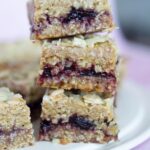 Stack of vegan oat bars filled with berry jam on a white plate, reminiscent of a delightful Cherry Bakewell treat.
