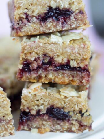 Stack of vegan oat bars filled with berry jam on a white plate, reminiscent of a delightful Cherry Bakewell treat.