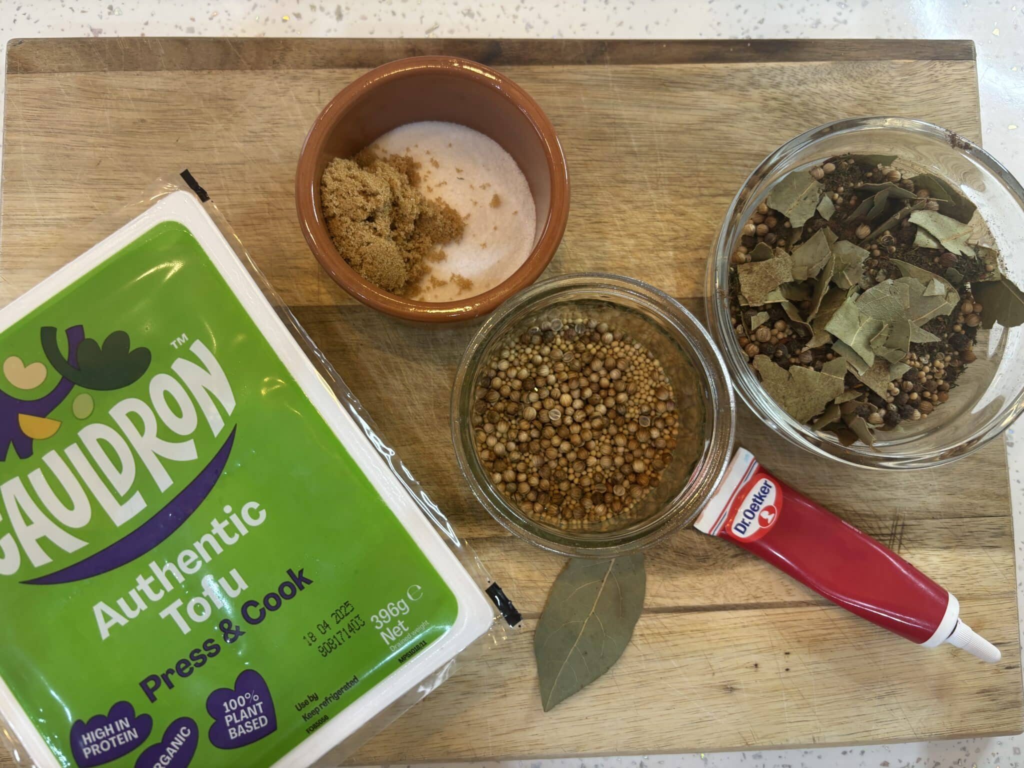 The Best Vegan Corned Beef Recipe (Made With Tofu) 128 A block of Cauldron tofu, a tube of tomato paste, brown sugar and salt in a small bowl, whole spices, and bay leaves on a wooden cutting board.