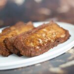 Two slices of vegan corned beef topped with melted cheese are served on a white plate.