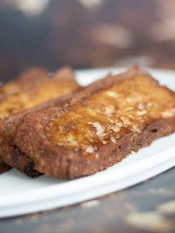 Two slices of vegan corned beef topped with melted cheese are served on a white plate.