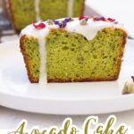 A slice of green Vegan Avocado Cake with lemon icing and flower petals on top, displayed on a white plate with the rest of the cake in the background. Text reads "Avocado Cake, Plant based.