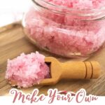 A jar of pink Cherry scrub sits on a wooden tray with a small wooden scoop holding some scrub in front. Text reads, "Make Your Own Cherry Body Scrub for gentle body exfoliation.