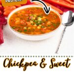 A bowl of Vegan Chickpea Soup sits on a table with a spoon beside it, surrounded by fresh vegetables. A label indicates this easy vegan recipe is high in protein.