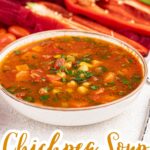 A bowl of chickpea soup garnished with herbs, surrounded by fresh vegetables like celery, sweet potato, bell pepper, and cherry tomatoes. Text reads "Chickpea Soup Vegan Meal Prep.