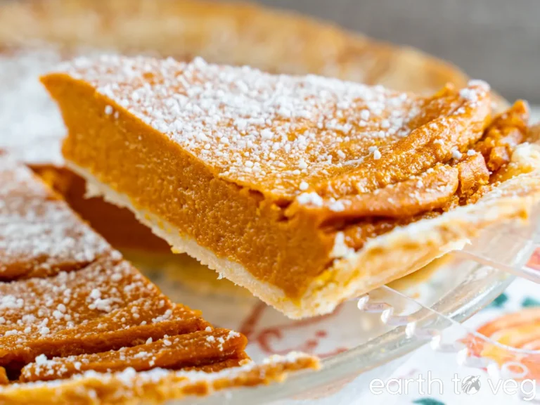Vegan Thanksgiving Desserts - Go-To Best Dessert Recipes 15 A slice of pumpkin pie with a dusting of powdered sugar being lifted from a glass pie dish-perfect for anyone searching for the best dessert recipes or looking to add vegan Thanksgiving desserts to their holiday table.